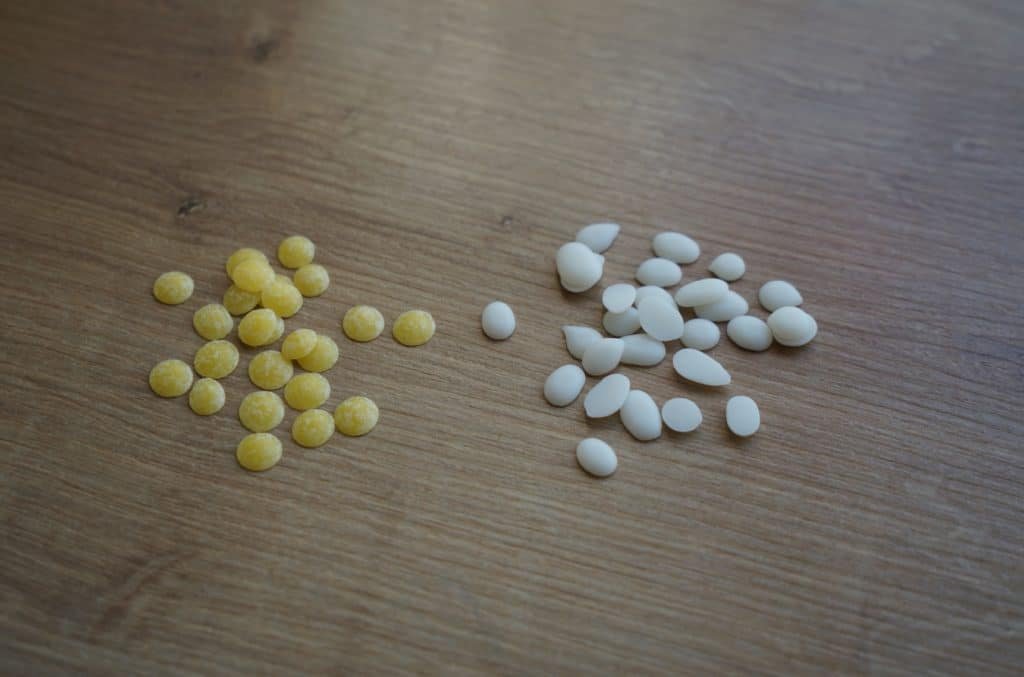 a handful of beeswax pastilles and rapeseed wax pastilles lying on a wooden surface