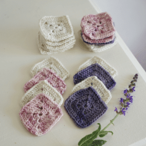 pink, white and purple crochet squares on a white surface and a purple salvia