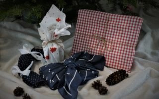 several gifts all wrapped in fabric on a blanket along with some pine cones