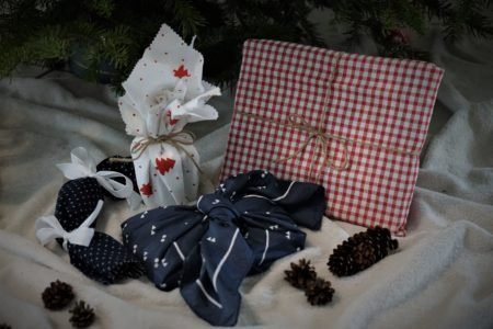 several gifts all wrapped in fabric on a blanket along with some pine cones