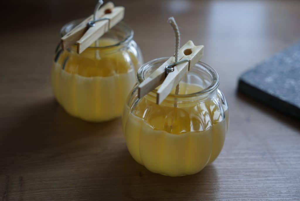 two freshly poured beeswax candles with wicks secured by clothespins