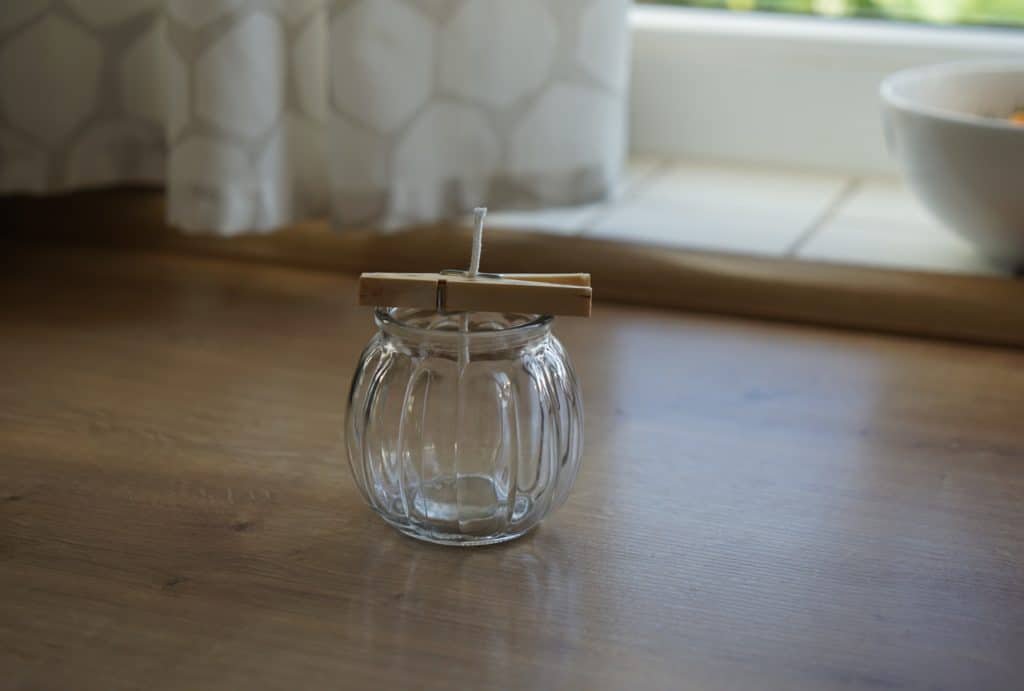 empty glass jar with a wick secured by a clothespin