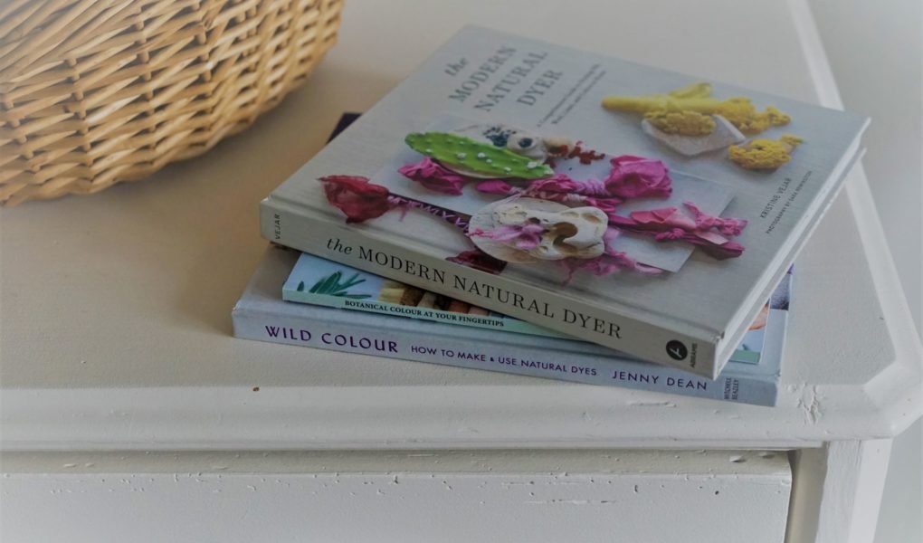 three books on botanical dyeing on a white wooden dresser next to a wooden basket
