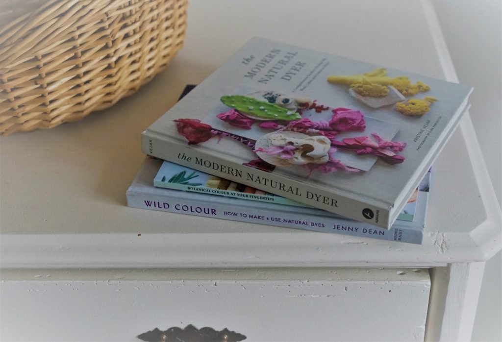three books on botanical dyeing on a white wooden dresser next to a wooden basket