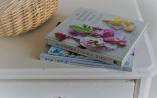 three books on botanical dyeing on a white wooden dresser next to a wooden basket
