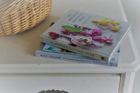 three books on botanical dyeing on a white wooden dresser next to a wooden basket