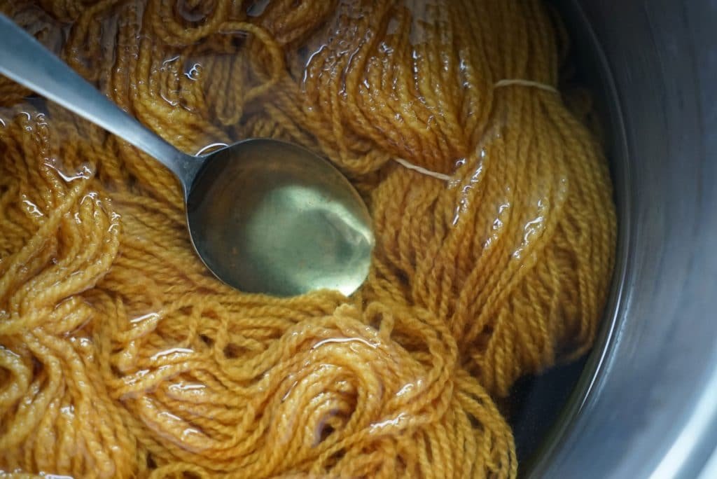 orange yellow skein of yarn and a spoon in a pot with a onion dye solution