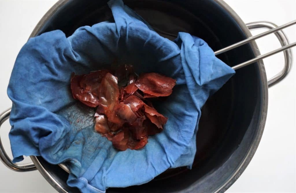 onion skins in a blue piece of fabric over a sieve and a pot