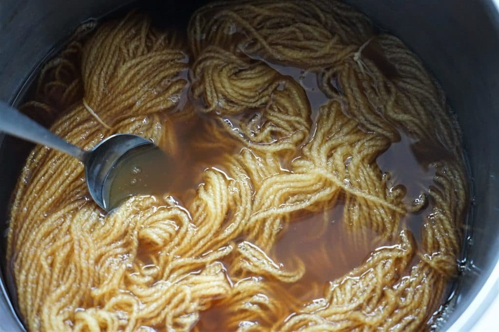 skein of yarn and a spoon in a dye solution in a pot