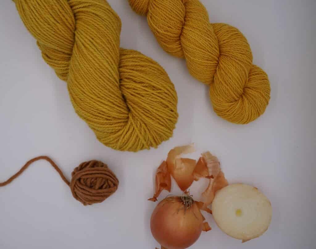 two skeins of yellow yarn and a ball of rust yarn and some onions and skins