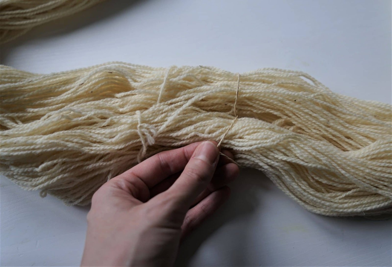 undyed hank of yarn and a hand tying a piece of package cord around the yarn