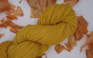 yellow skein of yarn naturally dyed with onion skins and some onion skins in the background