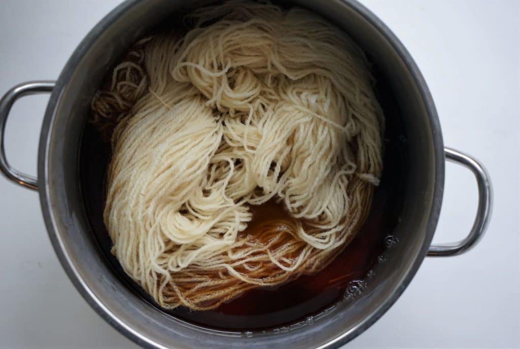 natural skein of yarn in a pot with brown/orange coloured dye solution