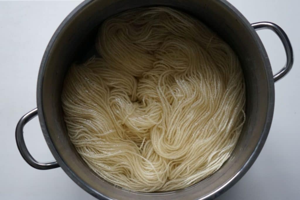 undyed cream skein of yarn in a pot with water