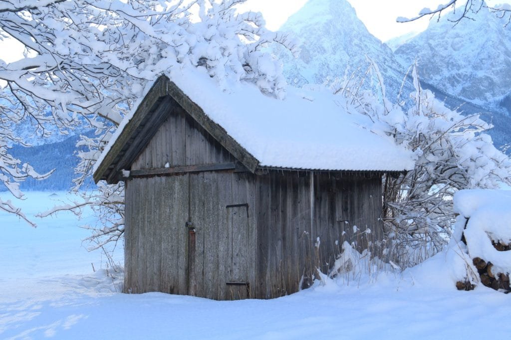 wooden shed covered in snow in front of the mountains