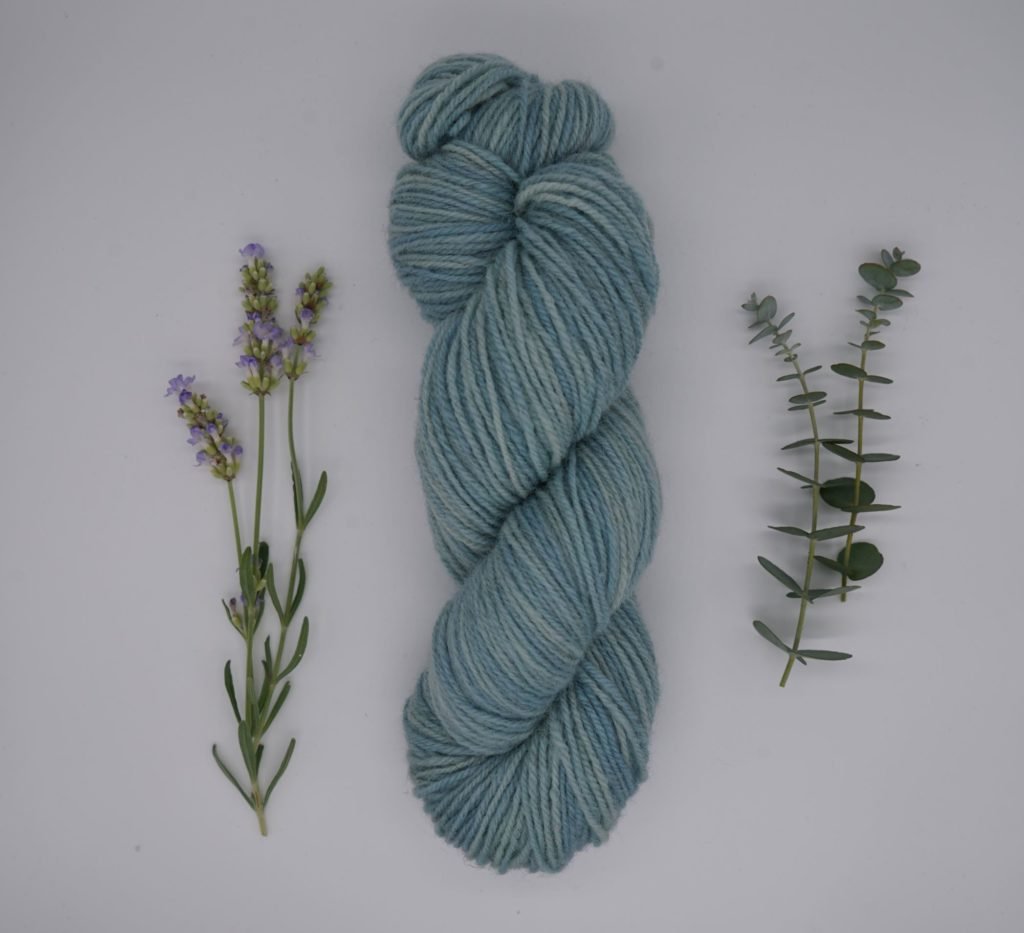 one blue skein of yarn alongside an eucalyptus branch and a lavender branch