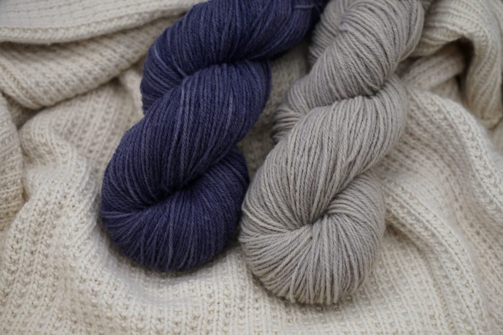 one grey and one blue skein of yarn on top a white woolen background