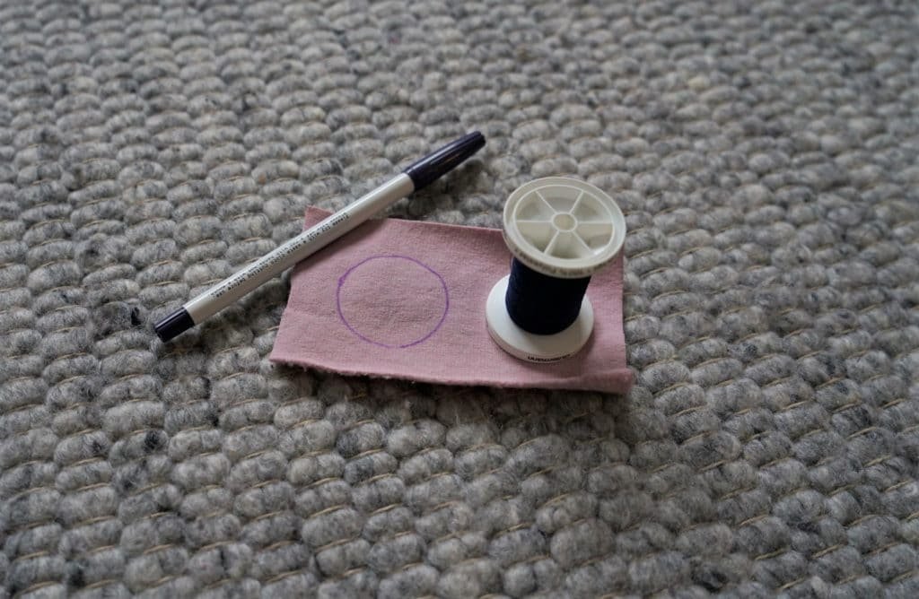a marker, spool and a pink piece of scrap fabric with a circle drawn onto it