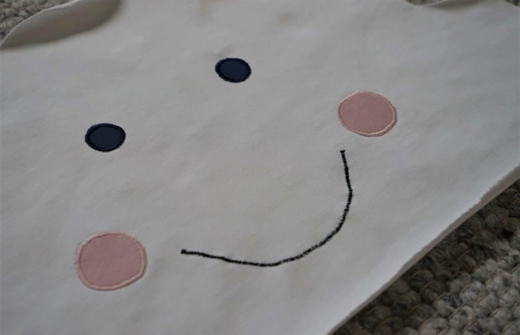 a cloud shape drawn onto a white fabric with eyes, cheeks and a mouth appliquéd on it