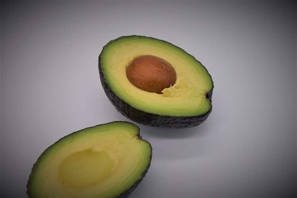 two pieces of a freshly cut avocado including the pit