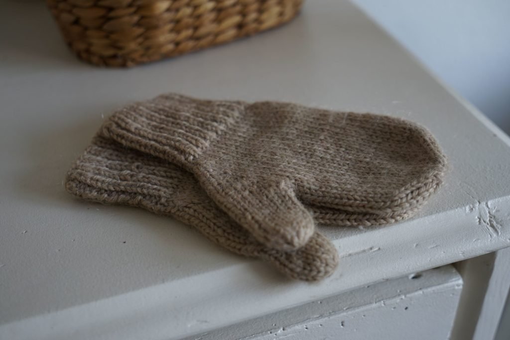 beige mittens on a white sideboard and a wooden basket in the background