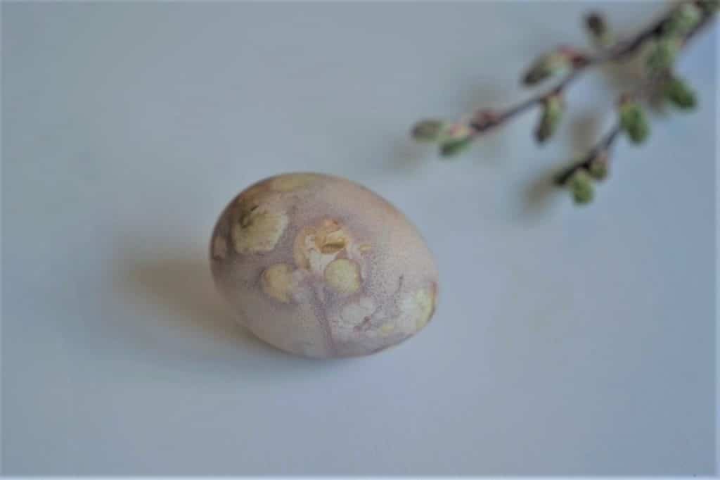 a patterned easter egg in soft yellow and purple tones and some branches in the background