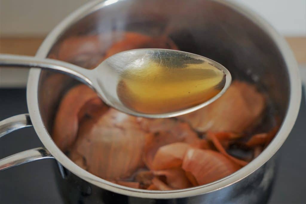 a spoon with a yellow liquid over a pot filled with yellow onion skins