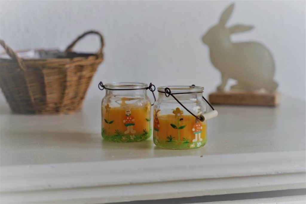 two yellow candles with easter bunnies in the front and a wooden basket and easter bunny decoration in the backgorund