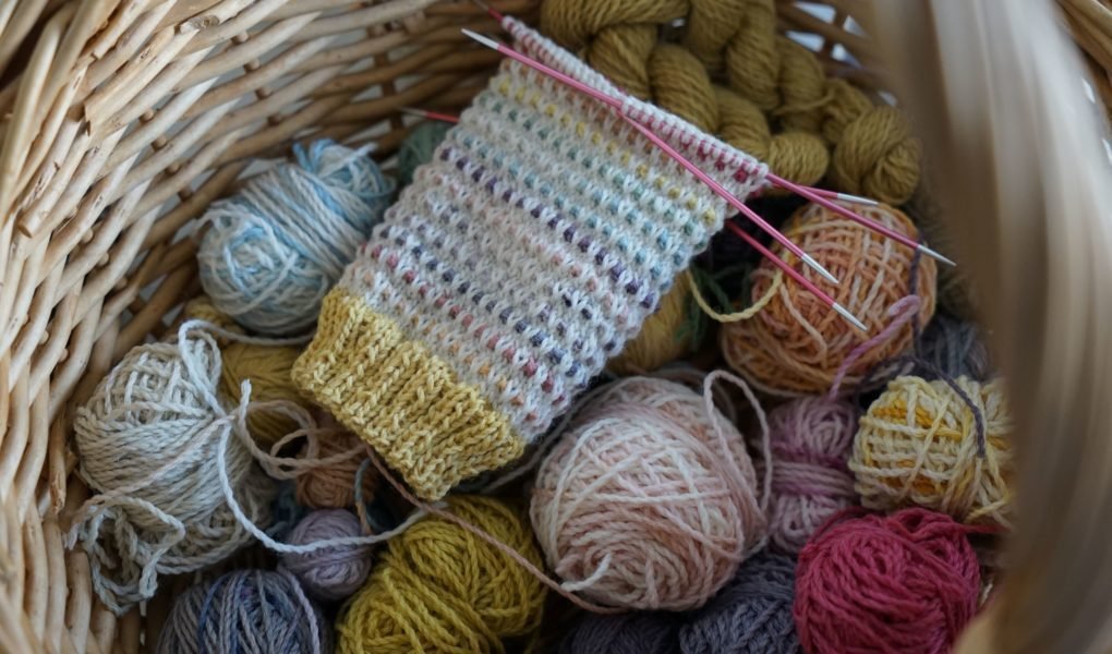a colourful sock in progress and lots of little balls of yarn in a basket