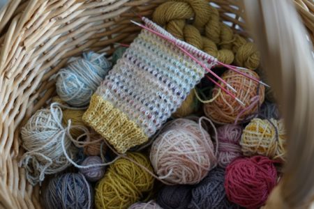 a colourful sock in progress and lots of little balls of yarn in a basket