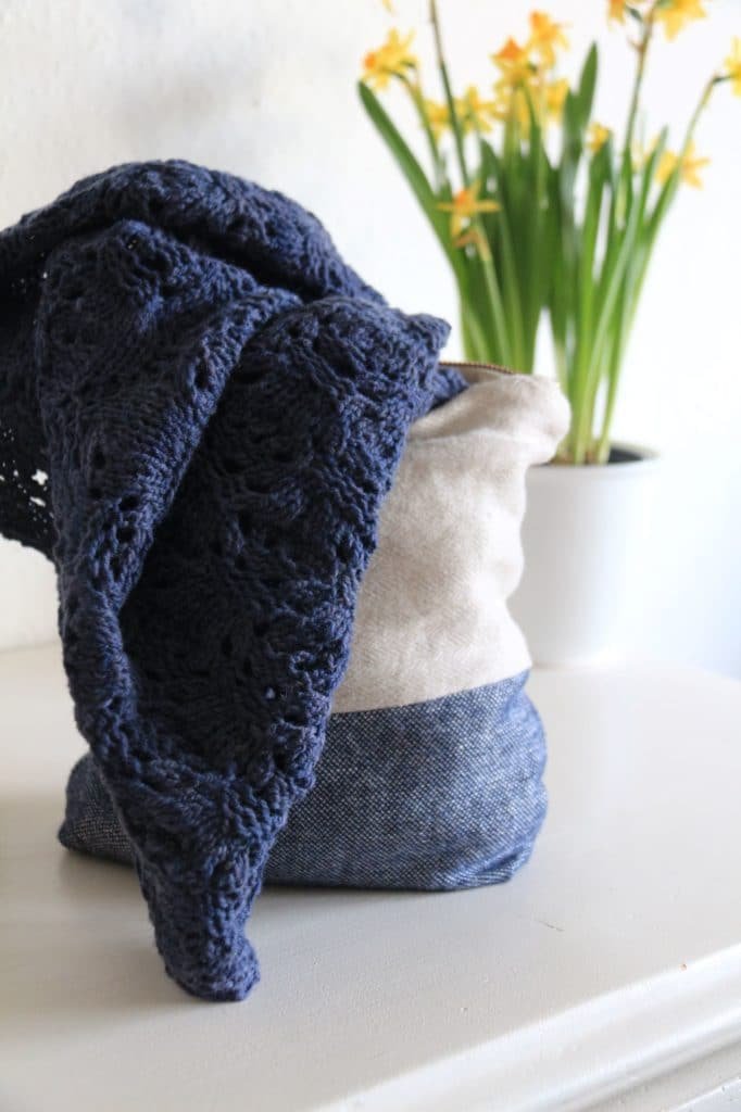 a dark blue piece of knitwear peeking out of a bag in front of some daffodils on a white sideboard