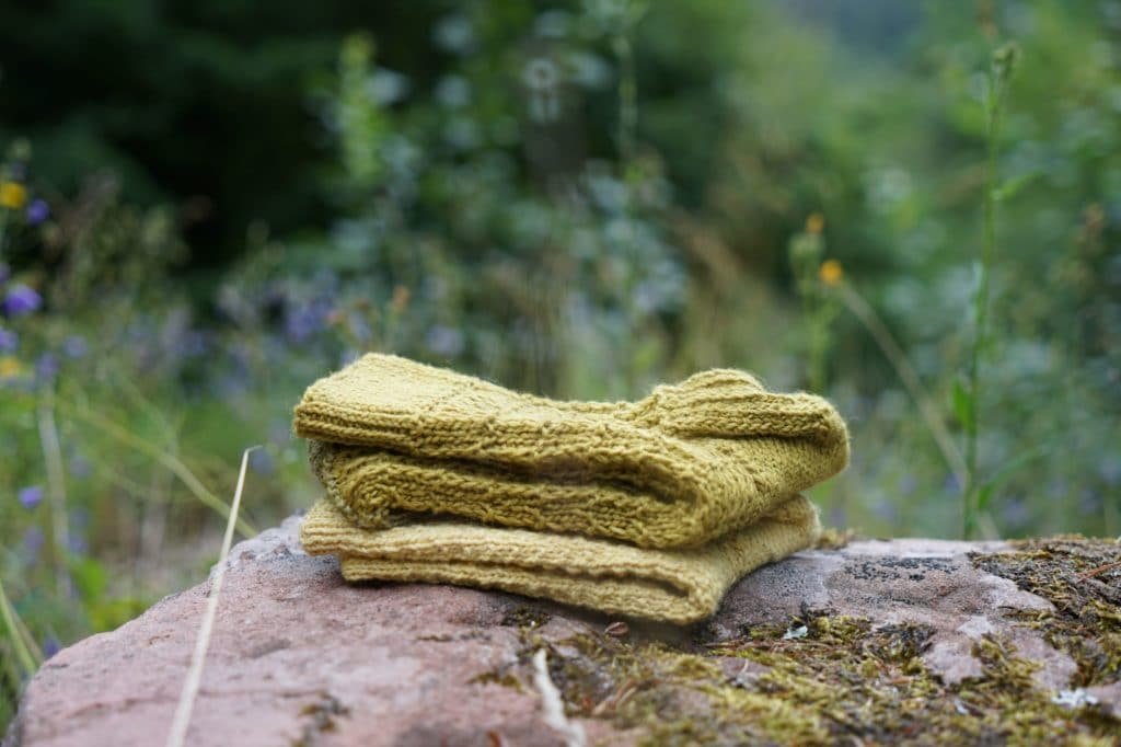 green and yellow socks on a rock in the woods naturally dyed with pine needles