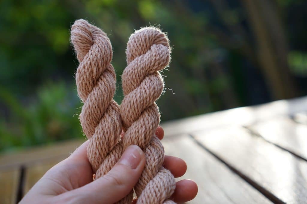 two mini skeins of apricot colored yarn held by a hand