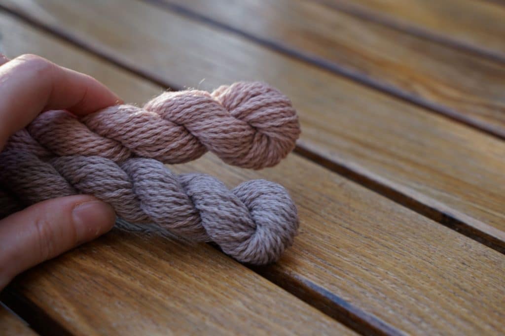 two skeins of yarn on a wooden surface held by a hand
