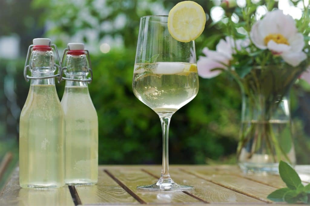 two glass bottles of elderflower syrup and a glass with a cocktail containing elderflower syrup