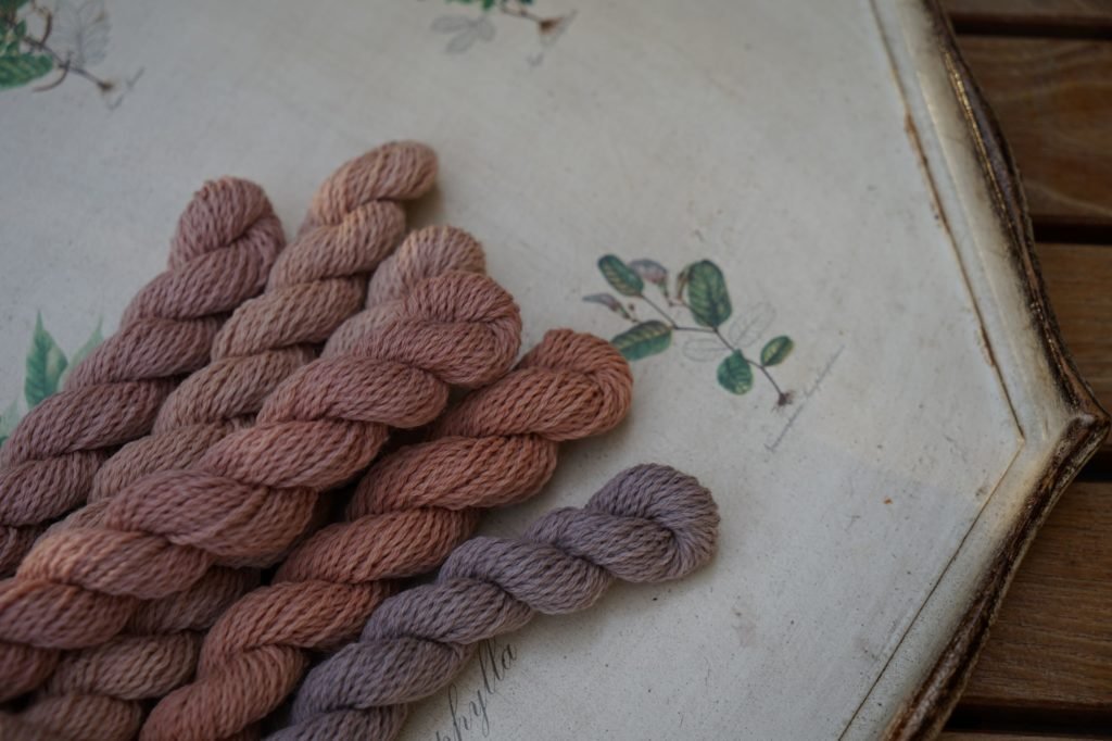 six mini skeins of yarn in different shades of peach, apricot, mauve and dusty pink on a tablet with flower design