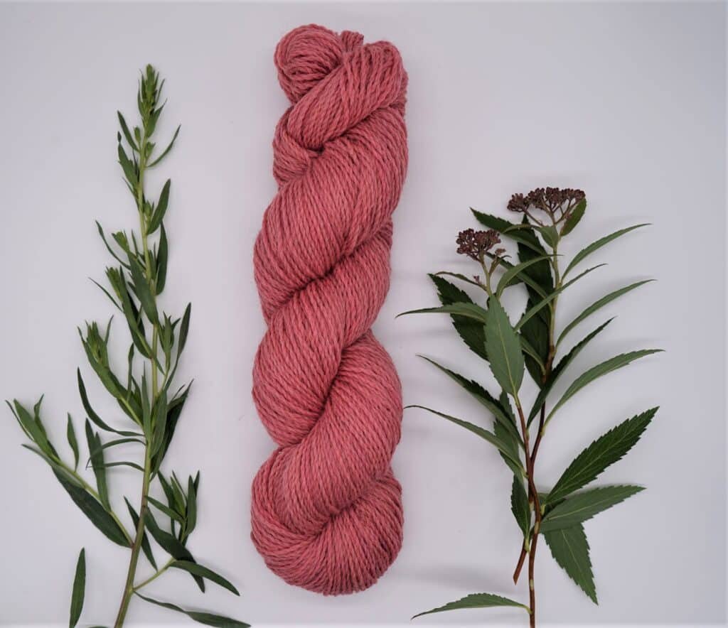 one coral pink naturally dyed skein of yarn alongside some flowers