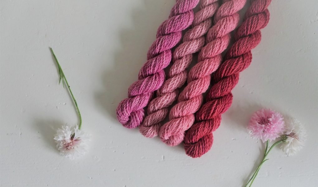 four pink mini skeins of yarn and some white and pink flowers