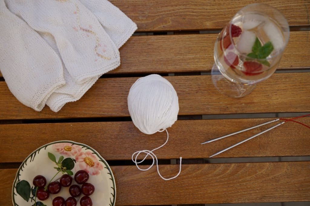 summer table with cherries, a cocktail and a cotton bamboo yarn knitting project