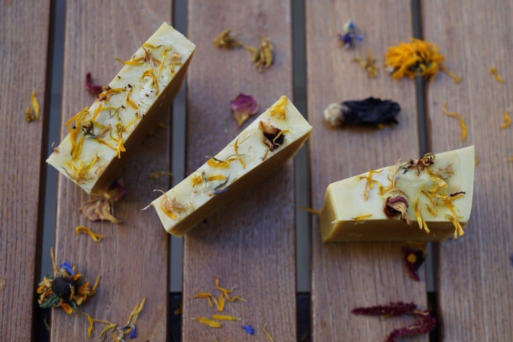 three pieces of cold process soap topped with dried flowers on a wooden surface