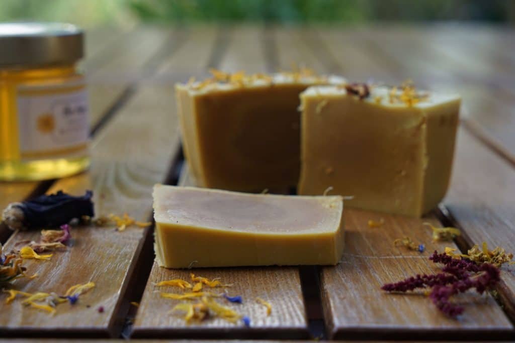 three pieces of goldenrod honey soap with a glass of honey and dried flowers on a wooden surface