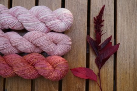 three skeins of yarns in pink shades and an amaranth hopi red dye on a wooden surface