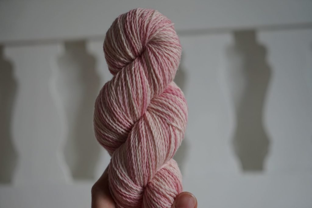 a skein in light pinks and white held by a hand