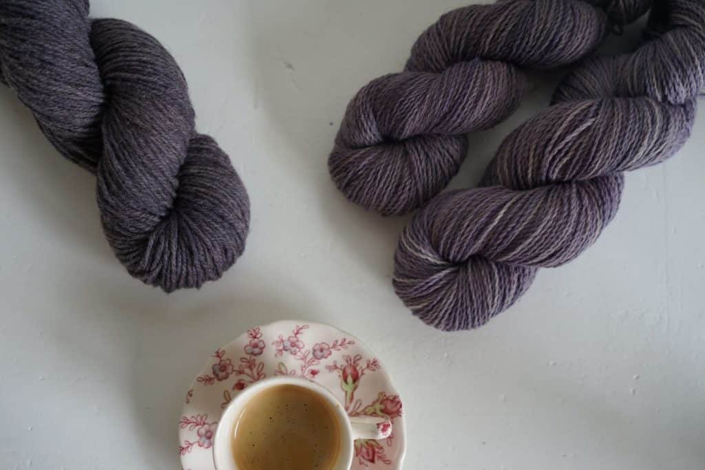 three purple skeins of yarn and a cup of espresso