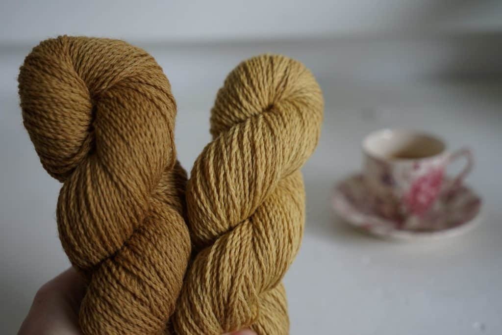 two brown skeins of yarn and a floral cup of espresso in the background