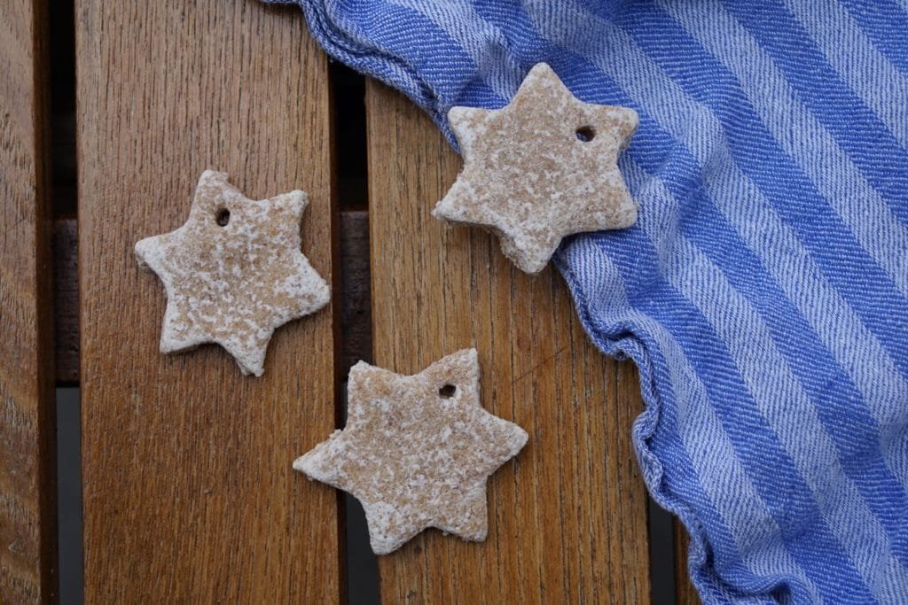 essential oil star ornaments made from play dough next to a blue striped kitchen towel on a wooden table