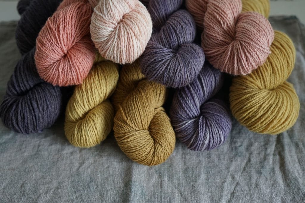 stacks of yarn skeins in browns, purples and pinks on a grey linen