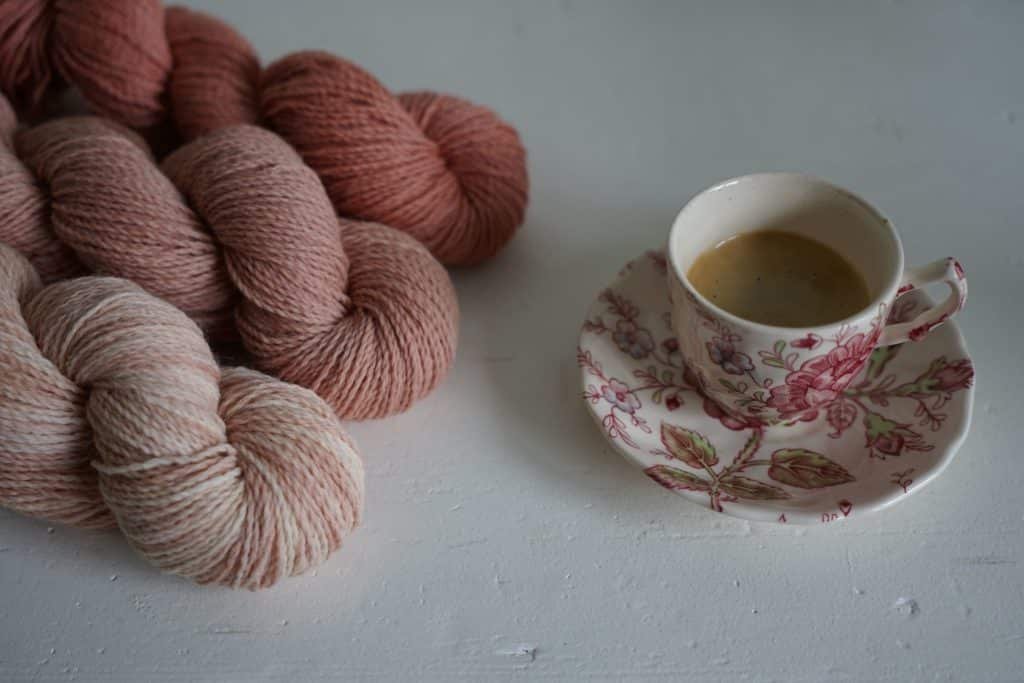 three pink skeins of yarns next to a floral cup of espresso
