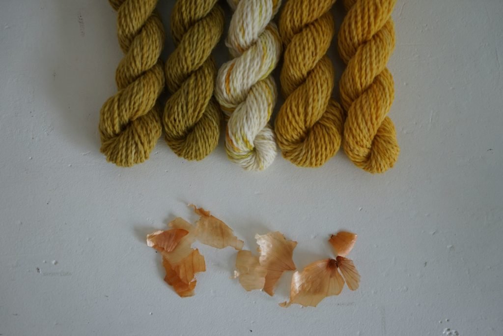 five mini skeins of yarn naturally dyed with onion skins and some yellow onion skins