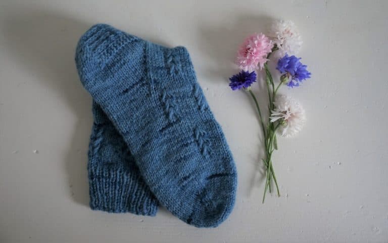 a blue hand knitted song a some flowers next to it